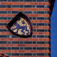 Coat of arms with a lion, standing upright, on the brick wall of the town hall of Lüneburg, decorated with blue and red clinkers
