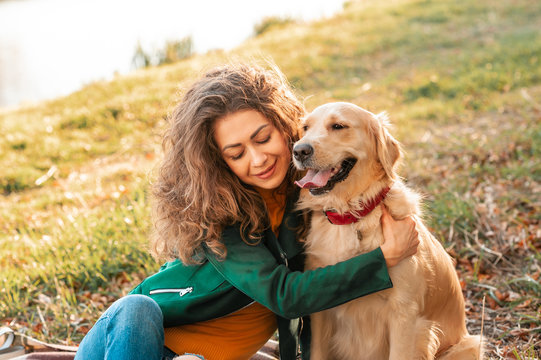 Smiling woman hugging her pet golden retriever dog near face. Golden retriever dog playing with a curly woman walking outdoors sunny day. love and care for the pet.