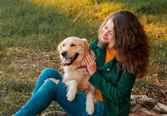 Smiling woman hugging her pet golden retriever dog near face. Golden retriever dog playing with a curly woman walking outdoors sunny day. love and care for the pet.