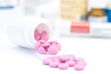 pink pills from a white jar on the background of many drugs. The concept of health care, treatment, illness.