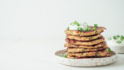 Zucchini fritters. Traditional zucchini fritters in stack on white background. Zucchini pancakes or fritters with green onion and parmesan cheese,served sour cream or greek yogurt. Banner. Copy space
