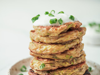 Zucchini fritters. Traditional zucchini fritters in stack on white background. Vegetable vegetarian zucchini pancakes or fritters with green onion and parmesan cheese,served sour cream or greek yogurt