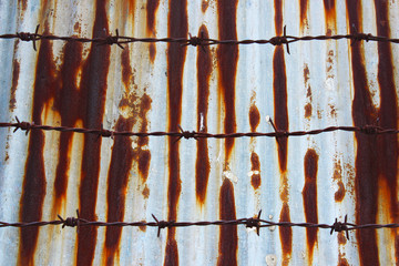 Rusty galvanized fence with rusty barbed wire in front