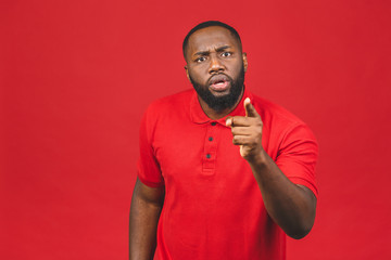 Crazy angry African American man pointing finger, looking at camera, mad young male quarreling, blaming anybody, shouting, feeling aggression, conflict concept, isolated over red background.