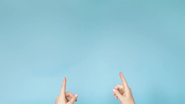 Female fingers pointing up on blue background. Girl advertises actively gesticulating on blue studio background. Copy space. 4k.