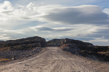 Northern country road among hills with colorful autumn tundra trees and bushes on a cloudy day. Travel to Teriberka. Kola Peninsula, Murmansk region, Russia