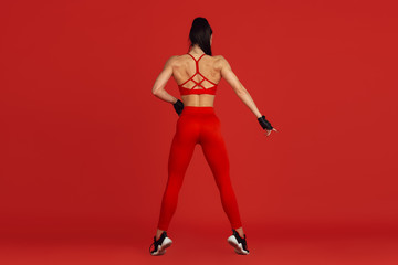 Fototapeta na wymiar Posing graceful. Beautiful young female athlete practicing in studio, monochrome red portrait. Sportive fit brunette model training. Body building, healthy lifestyle, beauty and action concept.