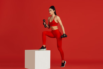Motion. Beautiful young female athlete practicing in studio, monochrome red portrait. Sportive fit brunette model with jump box and weights. Body building, healthy lifestyle, beauty and action concept