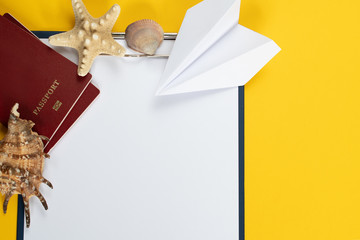 A reminder of what not to forget to take with you on a trip: tablet with pen, paper airplane, shell and starfish on a yellow background