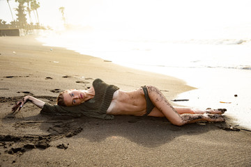 Beautiful sexy girl model lies on black sand beach, in a black swimsuit, with a tanned body, long blonde hair, magnificent breasts and puffy lips. Healthy nature, ocean waves, clouds on Bali island.