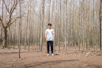 Obraz premium Asian Thai man in white casual stands alone in dry pie forest.