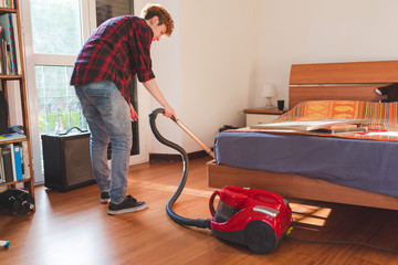 Fototapeta na wymiar Young gingerhead woman indoors at home cleaning using vacuum