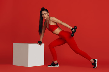 Motion. Beautiful young female athlete practicing in studio, monochrome red portrait. Sportive fit...