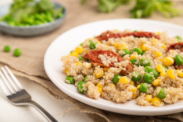 Quinoa porridge with green pea, corn and dried tomatoes on ceramic plate on a white wooden background. Side view, selective focus.