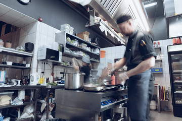 Fototapeta na wymiar Behind the scenes of brands. The chef cooking in a professional kitchen of a restaurant meal for client or delivery. Open business from the inside. Meals during the quarantine. Hurrying up, motion.