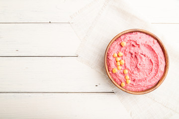 Hummus with beet in wooden bowl on a white wooden background. Top view, copy space.