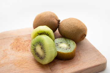 Closeup of ripe fresh whole and cut kiwi fruits on wooden chopping board isolated on white background. Organic food or healthy nutrition concept
