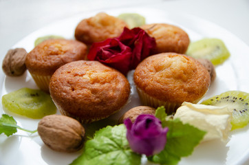 Tasty muffins on white plate on table with kiwi and flowers. Homemade bakery, selective focus. Plant-based food, vegetable muffins, sweet dessert