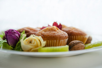 Tasty muffins on white plate on table with kiwi and flowers. Homemade bakery, selective focus. Plant-based food, vegetable muffins, sweet dessert