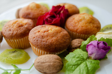 Tasty muffins on white plate on table with kiwi and flowers. Homemade bakery, selective focus. Plant-based food, vegetable muffins, sweet dessert