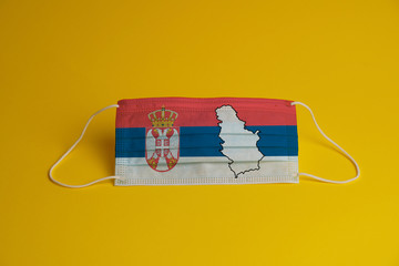 Coronavirus protective mask. Medical mask with Serbia flag and maps combined. Yellow background. Face mask protection against pollution, virus, flu. Healthcare and surgery concept.