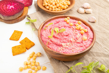 Hummus with beet and microgreen basil sprouts in wooden bowl on a white wooden background. Side view, close up.