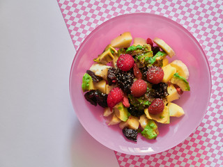 Italian breakfast with fresh fruit salad in pink bowl: avocado, raspberries, apple, banana, plums, almonds, goji berries and chia seeds