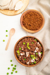 Quinoa porridge with green pea and chicken in wooden bowl on a white wooden background. Top view, close up.
