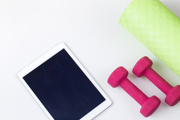 on the table is a tablet, dumbbells and a yoga mat 