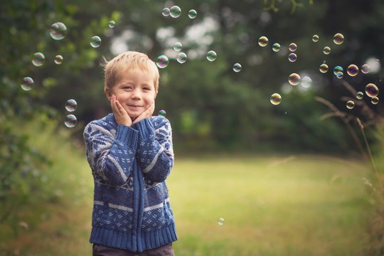 little boy is catching soap bubbles on the countyside and smiling