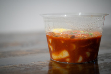 Blurry photo of a take out Korean food Stir-fried Rice Cake Tteok-bokki in microwaveable container.