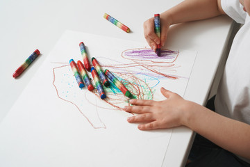 The child draws with wax crayons on paper. Close-up process of children's creativity. Development of creative abilities since childhood