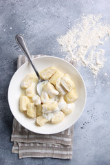 Russian and Ukrainian cuisine. Lazy dumplings with sugar, butter and sour cream in a white plate with a spoon on a light grey background. Flatlay, top view. Background image, copy space