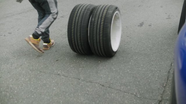 Mechanic rolls two new, freshly assembled wheels along the road close-up shot