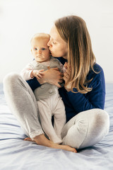 Fototapeta na wymiar Peaceful new mom hugging and kissing cute baby girl. Young woman nursing six month daughter in bedroom at home. Motherhood concept