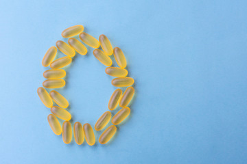 Soft chewable yellow jelly pills shaped as letter "O' as Omega 3. Capsules with yellow fish oil are lying on blue background. Health support and treatment concept. Biologically active additives.