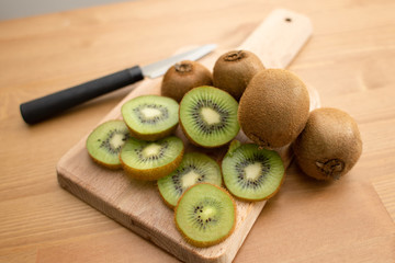 Whole and sliced kiwi fruits on chopping board and knife on wooden table surface. Healthy organic...