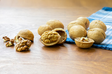 Whole walnuts and walnut kernel halves without shell on a dark wooden table and checkered towel, close up. Seeds of the common walnut tree Juglans regia. Macro food photo close up view.