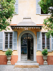 Fototapeta na wymiar Entrance to a beautiful yellow Italian villa with windows with gray shutters, decorated with flowerpots with greenery and pebbles on the floor