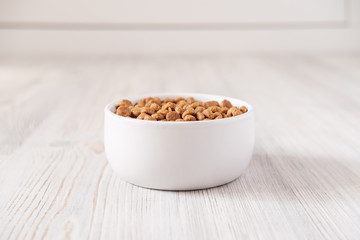 White, porcelain bowl with dry pet food is on the floor, on a blurred background. Copy space.