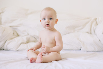 Cute smiling baby sits on the bed. happy naked baby.  children under one year old. baby girl playing, smiling, posing on the bed 