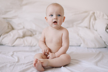 Cute smiling baby sits on the bed. happy naked baby.  children under one year old. baby girl playing, smiling, posing on the bed 