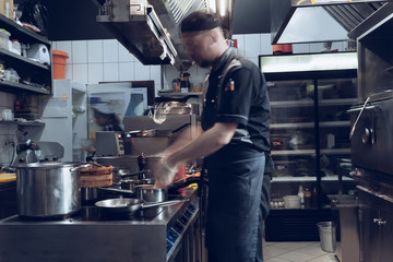 Behind the scenes of brands. The chef cooking in a professional kitchen of a restaurant meal for client or delivery. Open business from the inside. Meals during the quarantine. Hurrying up, motion.
