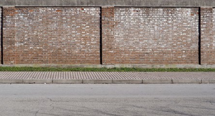 Urban street background. Old brick wall, a line of grass, a large sidewalk and an asphalt road