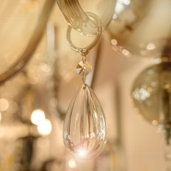 A fragment of the crystal decor of a drop hanging on the transparent glass armature of the ceiling chandelier in the interior. Concept of luxury design. Close up. Soft warm filter, selective focus.