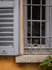 wine glasses standing on a window with gray shutters
