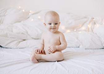 Cute smiling baby sits on the bed. happy naked baby.  children under one year old. baby girl playing, smiling, posing on the bed 