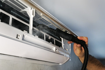 worker's hand holds brush from  portable steam generator for maintenance air condition split system, steaming for protection against dust, allergens, dirty air, microbes, healthcare concept