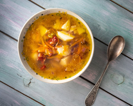 Homemade freshly prepared soup with smoked pork ribs in a deep plate and a tablespoon on a wooden turquoise table