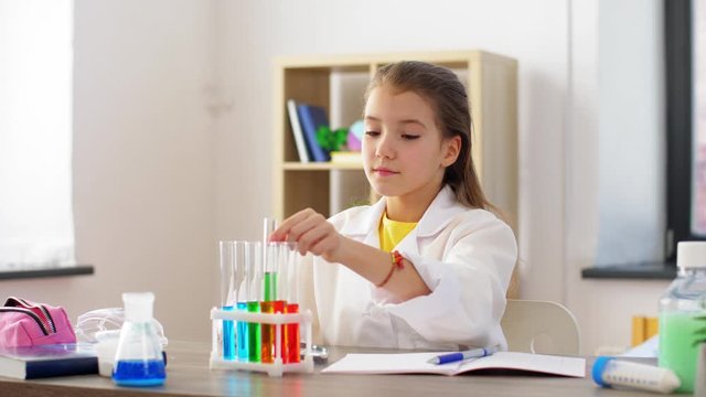 education, science and children concept - girl with magnifier studying test tube with chemical at home laboratory
